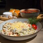 Appetizing Russian salad with fresh tomato and cheese, served with borscht and bread in a cozy outdoor setting.