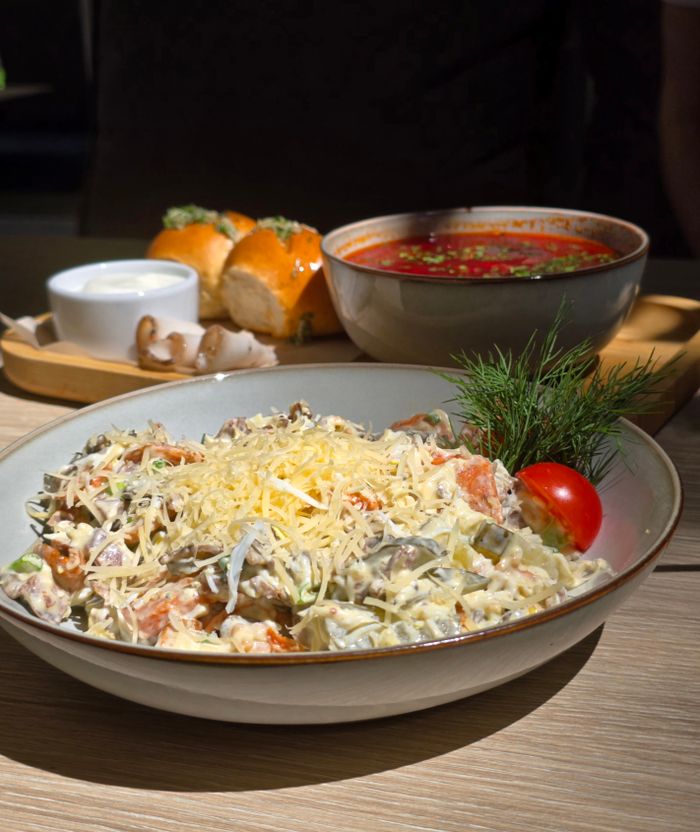 Appetizing Russian salad with fresh tomato and cheese, served with borscht and bread in a cozy outdoor setting.