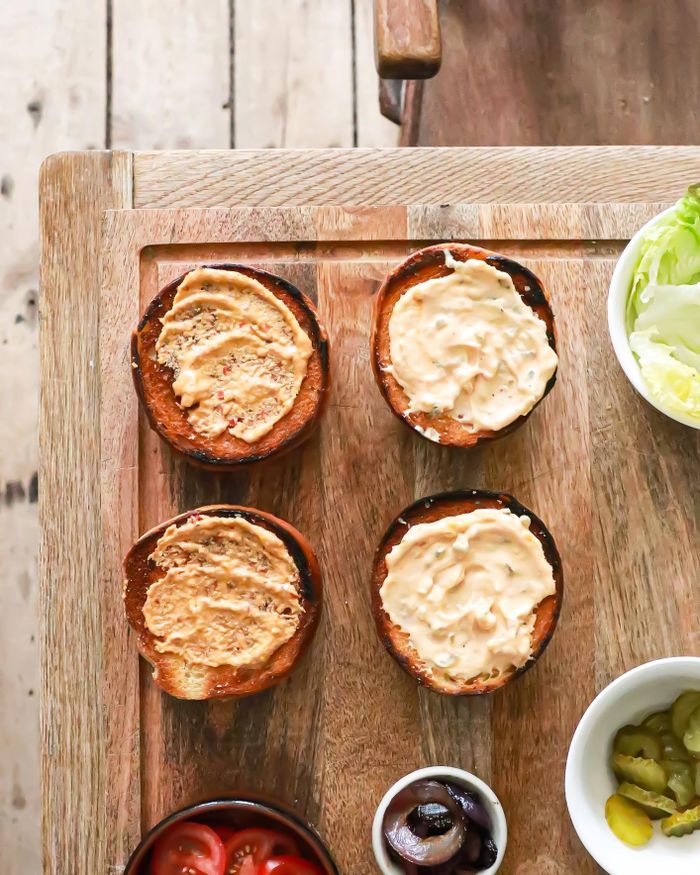 Top view of delicious toasted burger buns with sauces placed on wooden table with various ingredients while cooking process in kitchen