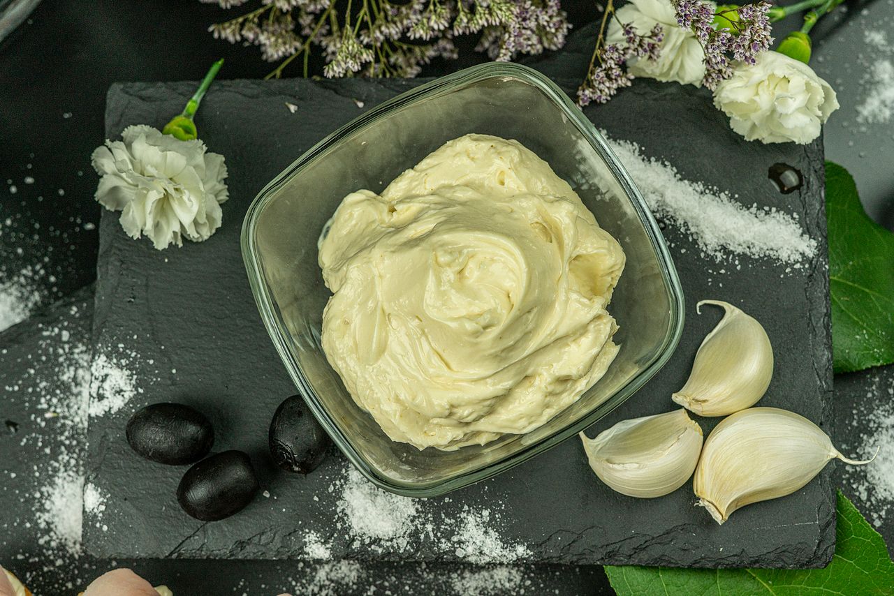 A creamy white sauce elegantly presented with garlic and olives on a slate board.